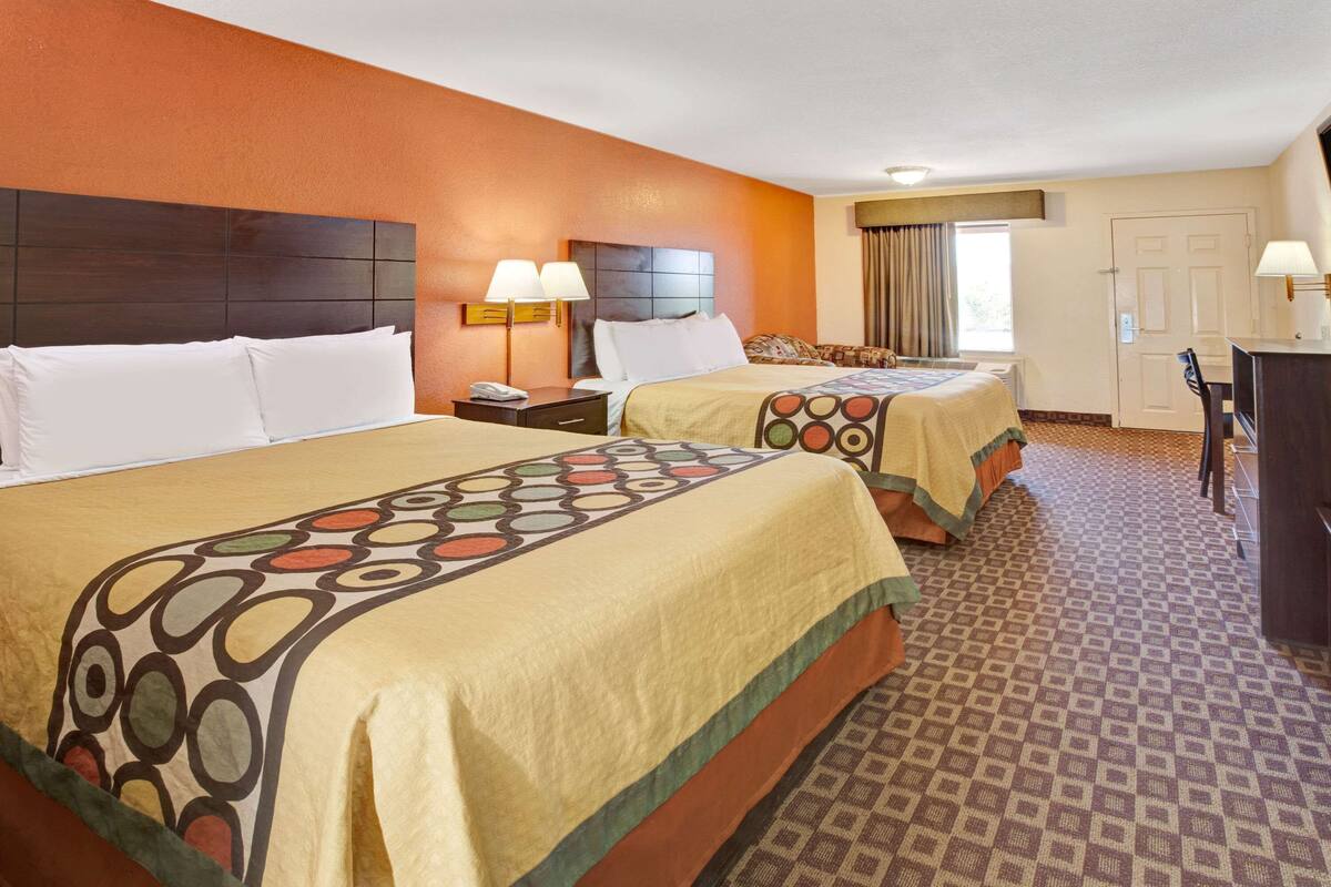 A hotel room with two beds, each with a headboard, bedside tables, lamps, and a patterned carpet.