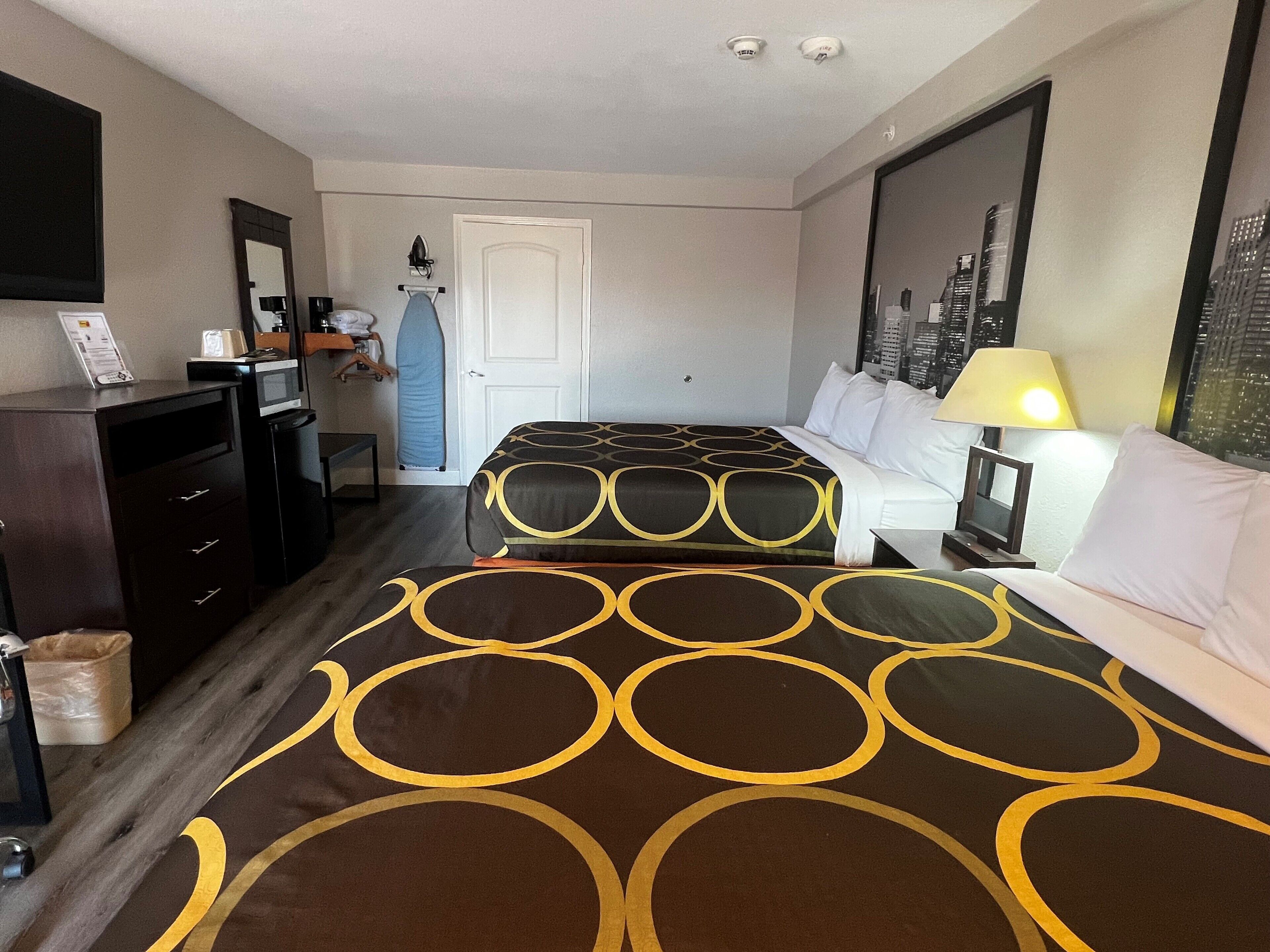 A hotel room with two beds, a desk, a chair, a mirror, a door, and a window with a cityscape view.