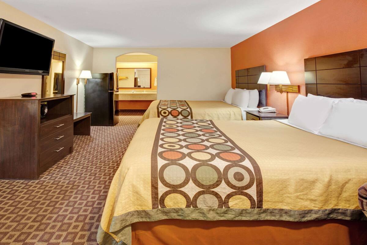 A hotel room with a large bed, a smaller bed, a desk, a TV, a dresser, and a bathroom with a mirror and towel rack.