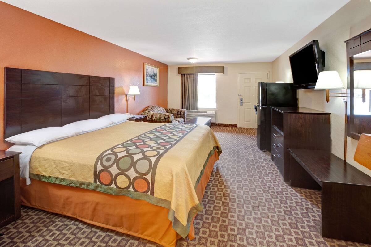A hotel room with a large bed, a desk, a TV, and a window with curtains.