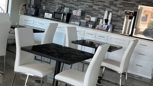 Eine moderne Küche mit weißen Schränken, einer schwarzen Arbeitsplatte und einer Rückwand aus Stein. Zwei weiße Stühle und ein schwarzer Tisch sind vorhanden.