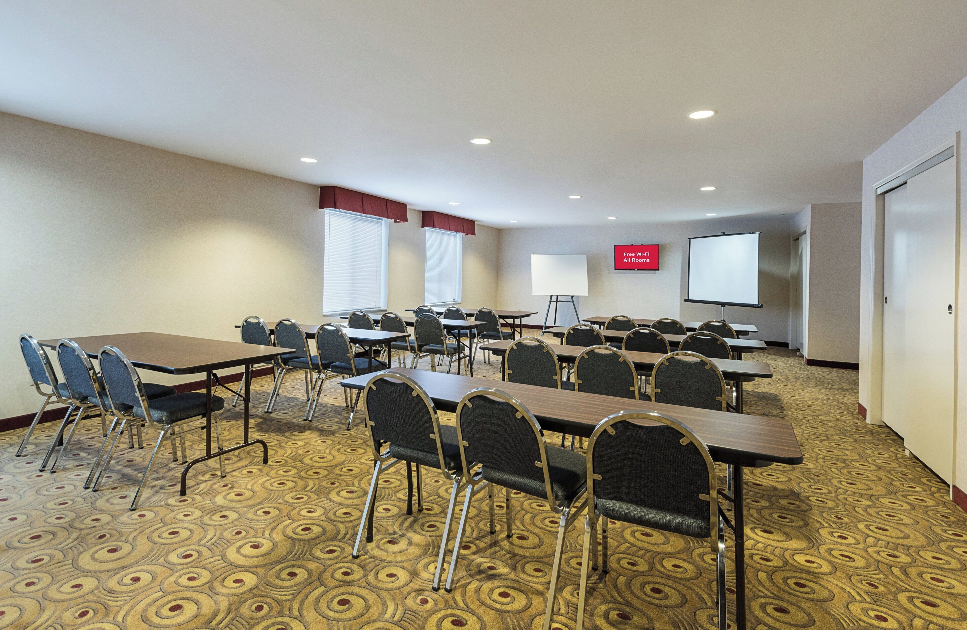 Una sala de conferencias con mesas, sillas, una pantalla de proyector y un cartel que indica acceso a Wi-Fi gratuito.
