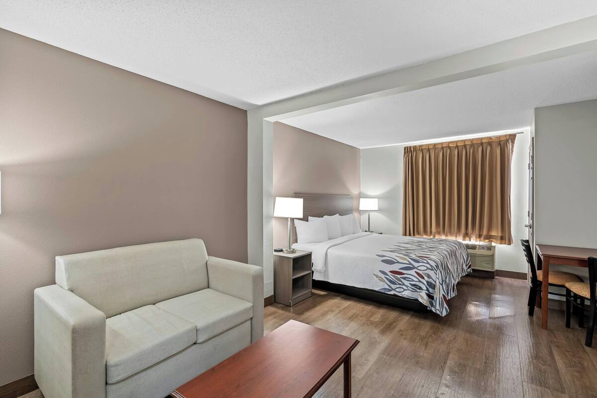 Een hotelkamer met een bed, een bank, een bureau, een lamp en een raam met gordijnen.