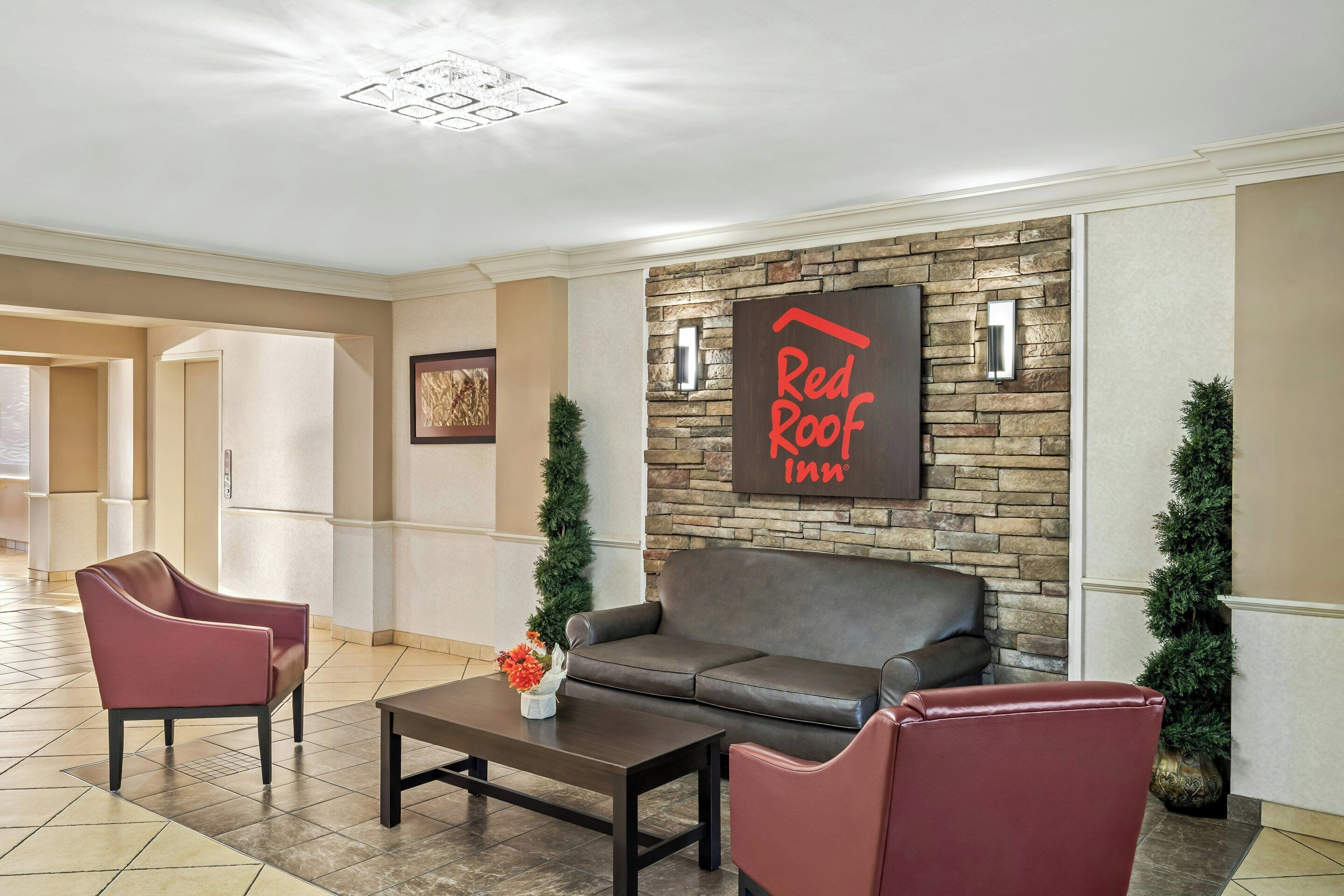 Un vestíbulo con pared de piedra, un letrero de Red Roof Inn, asientos de cuero y una mesa de centro.