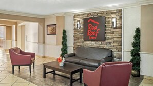 Un hall d’entrée avec un mur en pierre, un panneau indiquant un hôtel Red Roof Inn, des sièges en cuir et une table basse.