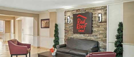 A lobby with a stone wall, a Red Roof Inn sign, leather seating, and a coffee table.
