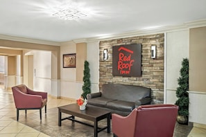Een lobby met een stenen muur, een Red Roof Inn bord, lederen zitplaatsen en een salontafel.