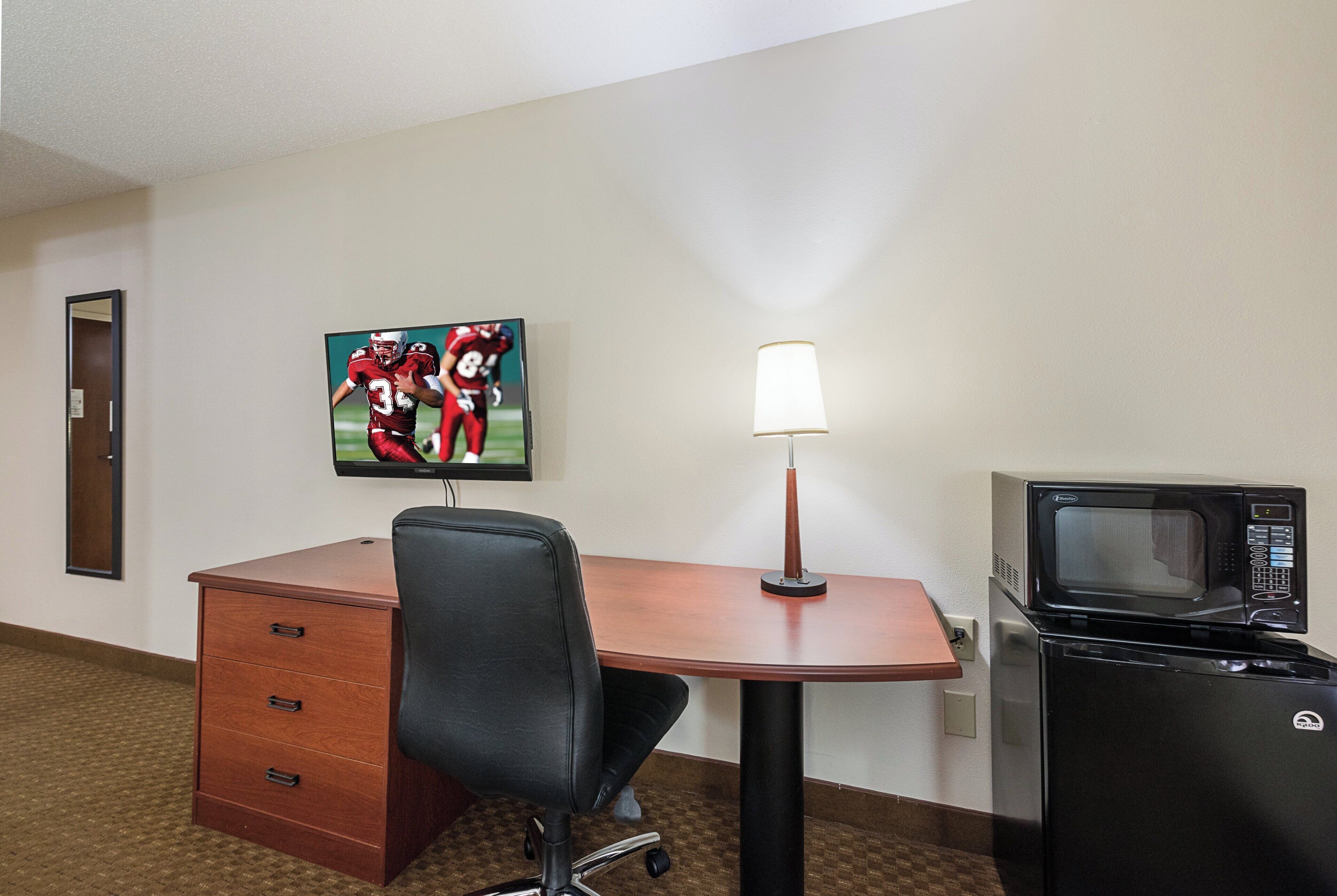 Habitación de hotel con escritorio, silla, lámpara y microondas.