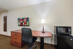 A hotel room with a desk, chair, lamp, and a microwave.