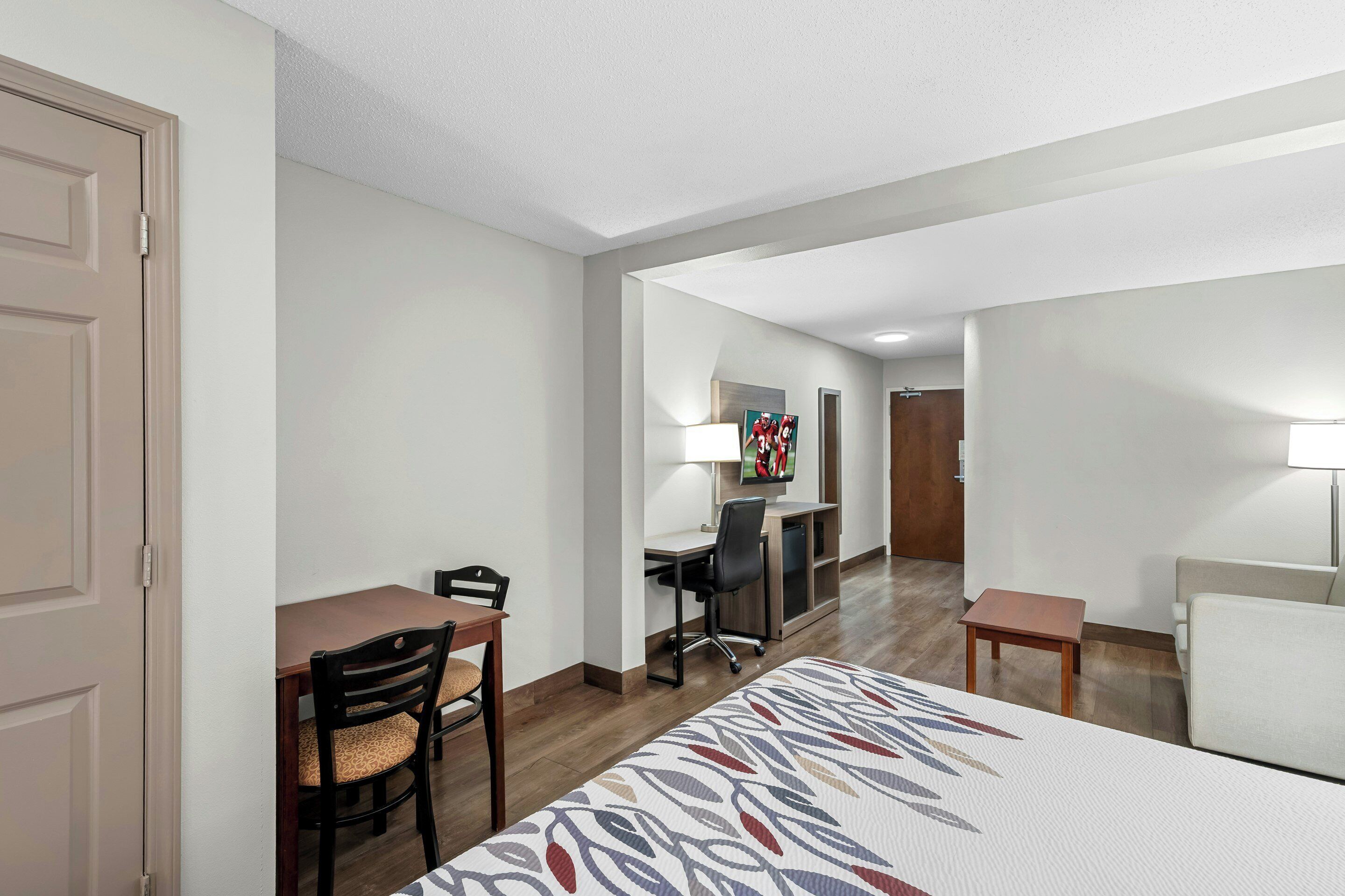 A hotel room with a bed, a desk, a chair, a TV, and a lamp.