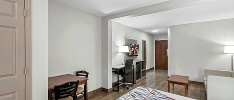 A hotel room with a bed, a desk, a chair, a TV, and a lamp.