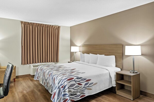 Una habitación de hotel con una cama, dos lámparas de noche, una silla, una mesita de noche y una ventana con cortinas.