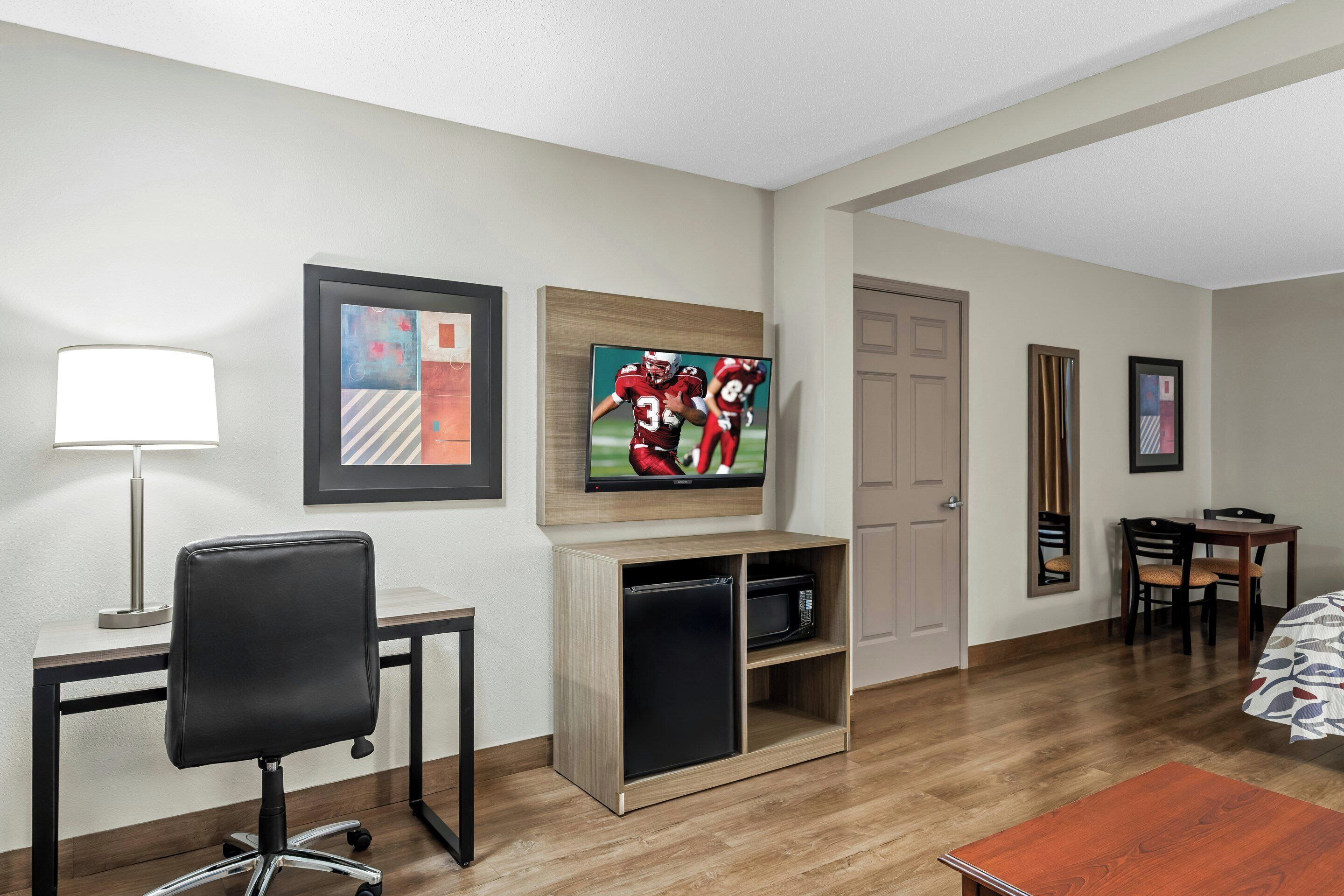 Una habitación de hotel con escritorio, silla, televisor, microondas y cama.