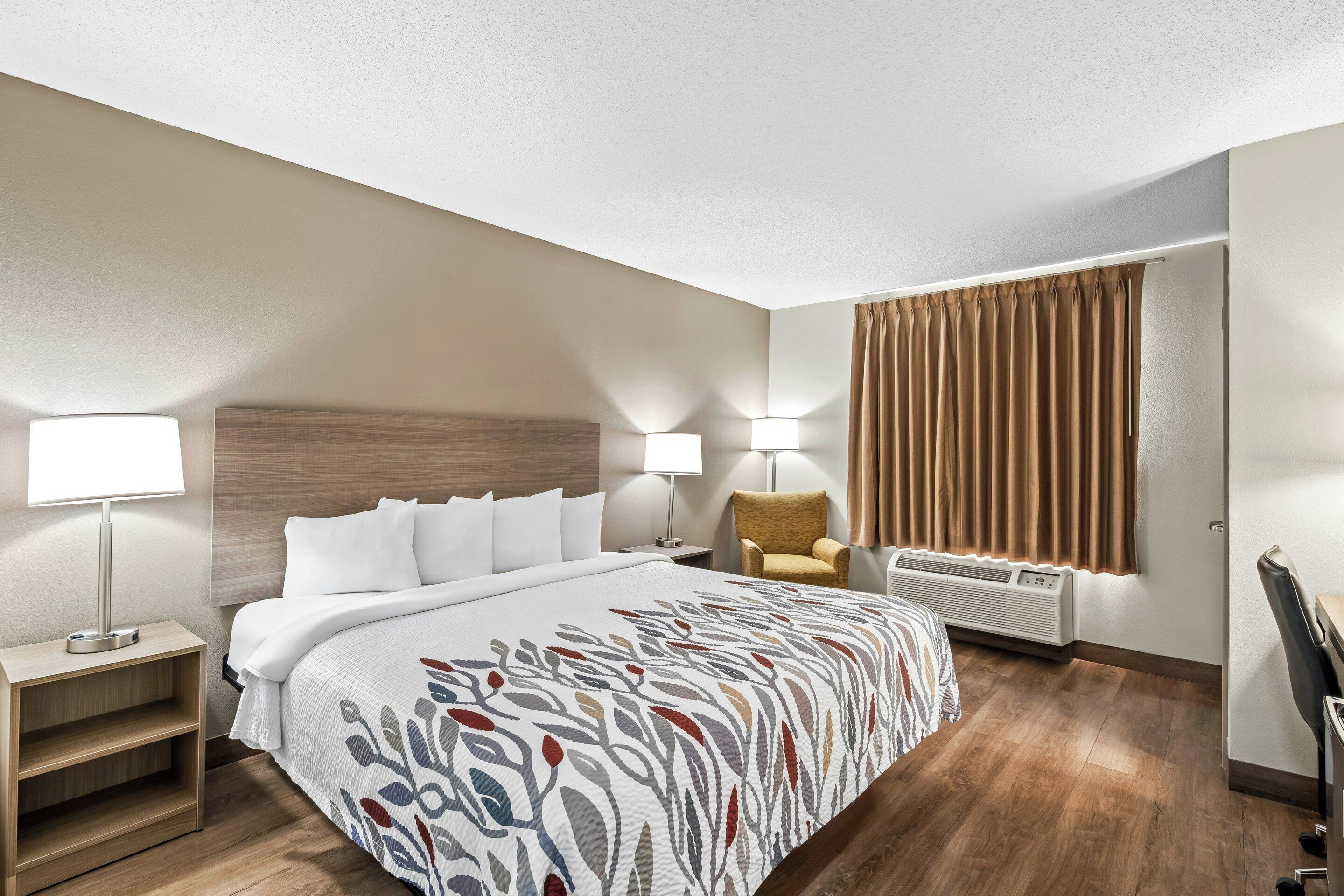 Habitación de hotel con cama, lámparas de noche, una silla, escritorio y ventana con cortinas.