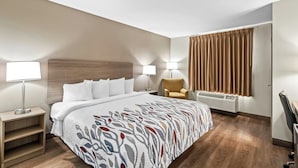 Une chambre d’hôtel avec un lit, des lampes de chevet, une chaise, un bureau et une fenêtre avec des rideaux.