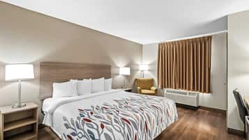 Habitación de hotel con cama, lámparas de noche, una silla, escritorio y ventana con cortinas.