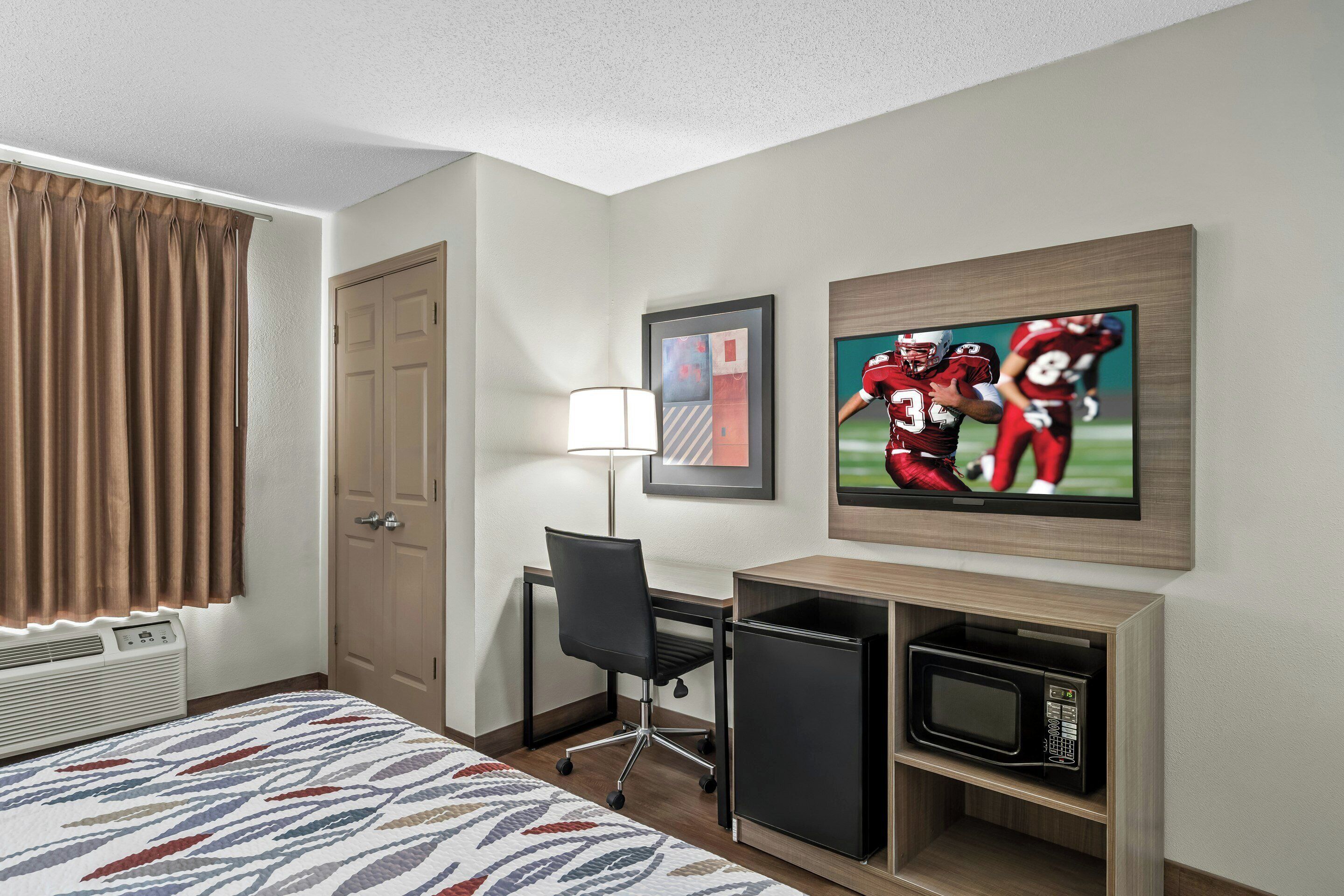 Habitación de hotel con cama, escritorio, silla, televisor y microondas.