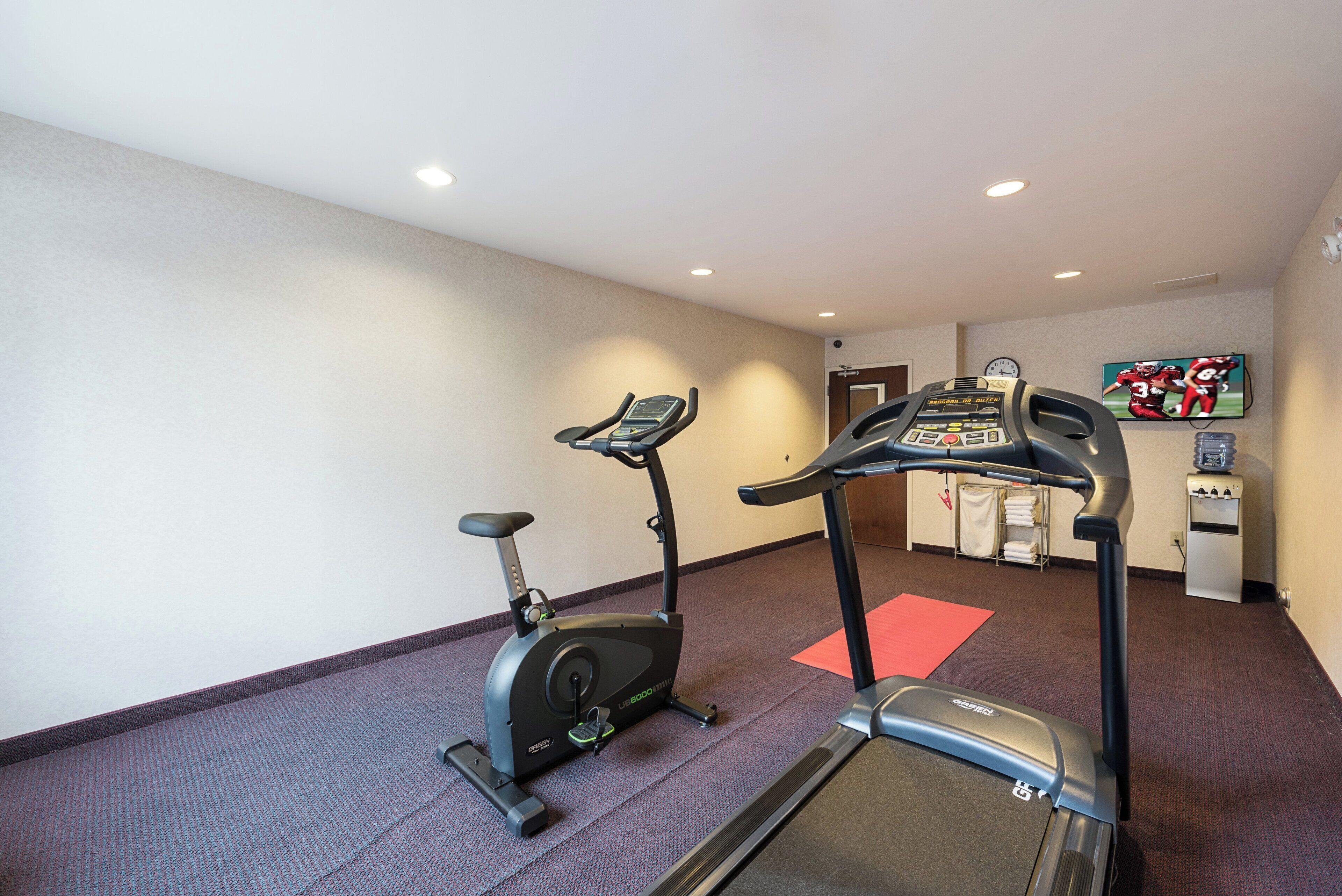 A hotel gym with two stationary bikes, a treadmill, and a water dispenser.