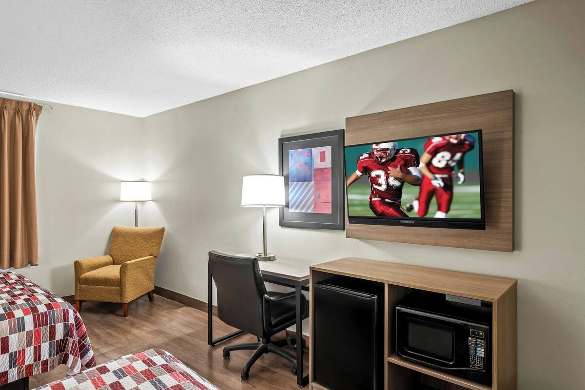 Een hotelkamer met een bed, een bureau, een stoel, een lamp, een televisie en een magnetron.