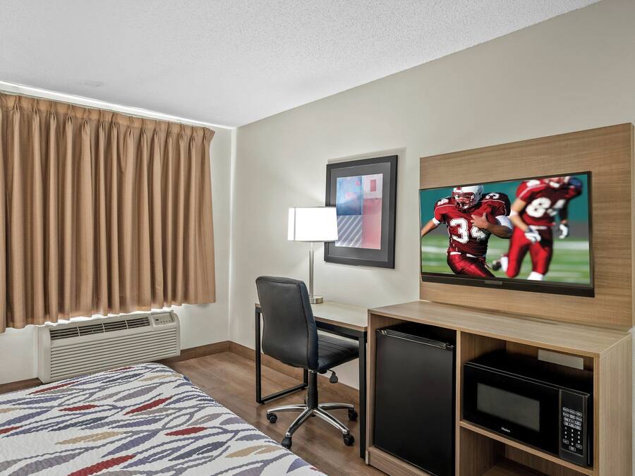 Una habitación de hotel con cama, escritorio, televisión y microondas.