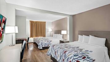 Habitación de hotel con dos camas, un escritorio, una silla, un televisor y una ventana con cortinas.
