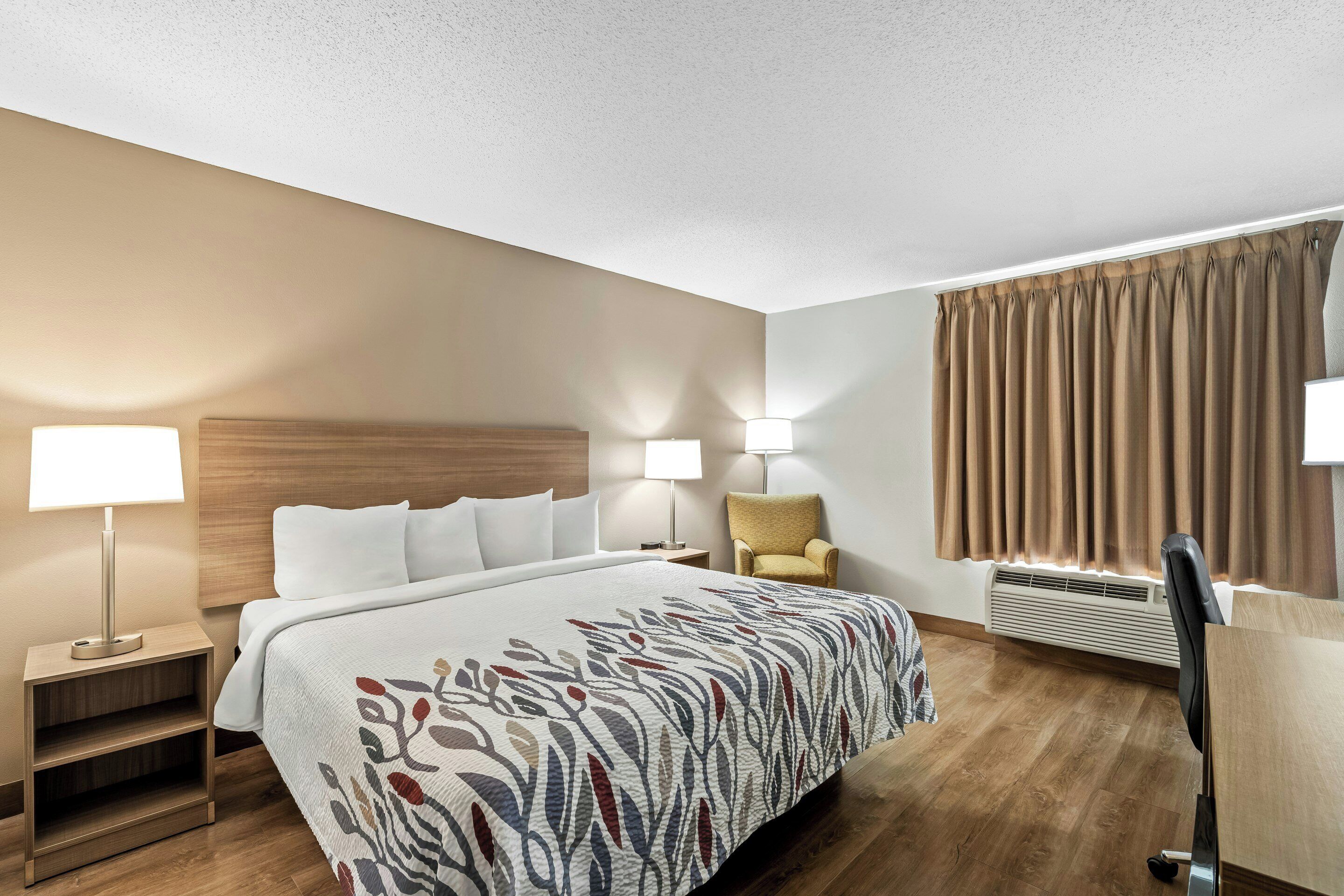 A hotel room with a large bed, two bedside lamps, a chair, a desk, and a window with curtains.