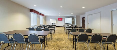 Una sala de conferencias con varias mesas y sillas, una pizarra, una pantalla de proyector y un cartel que indica acceso a Wi-Fi gratuito.