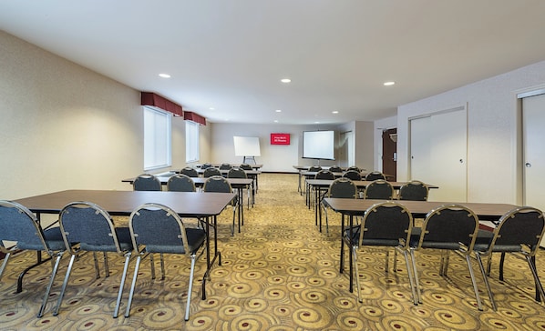 Una sala de conferencias con varias mesas y sillas, una pizarra, una pantalla de proyector y un cartel que indica acceso a Wi-Fi gratuito.