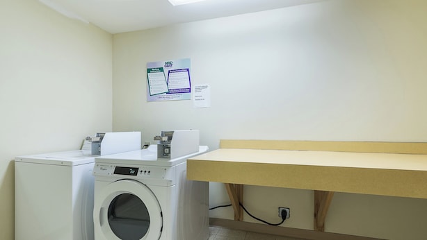 A laundry room with a front-loading washer and dryer, a wooden bench, and a wall-mounted sign with washing instructions.