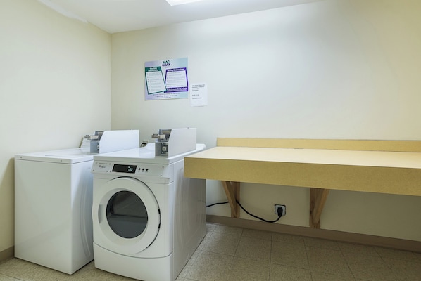 A laundry room with a front-loading washer and dryer, a wooden bench, and a wall-mounted sign with washing instructions.