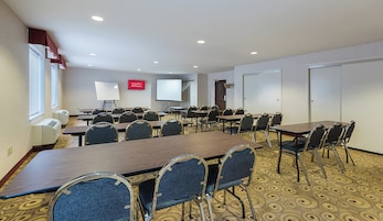 Un salón de conferencias con varias mesas y sillas, una pizarra, una pantalla de proyector y unidades de aire acondicionado.