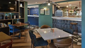 A modern hotel lobby with a reception desk, seating area, and bar.