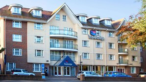 Hotel Travelodge com várias varandas, fachada de tijolos e área de estacionamento com carros.