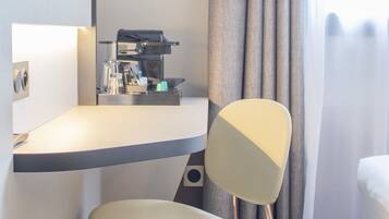 A modern hotel room with a minimalist design, featuring a desk with a coffee machine, a chair, and a bed.