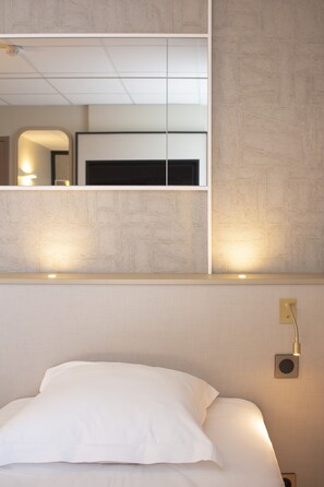 Une chambre d’hôtel avec un lit, un miroir fixé au mur et une lampe de chevet.