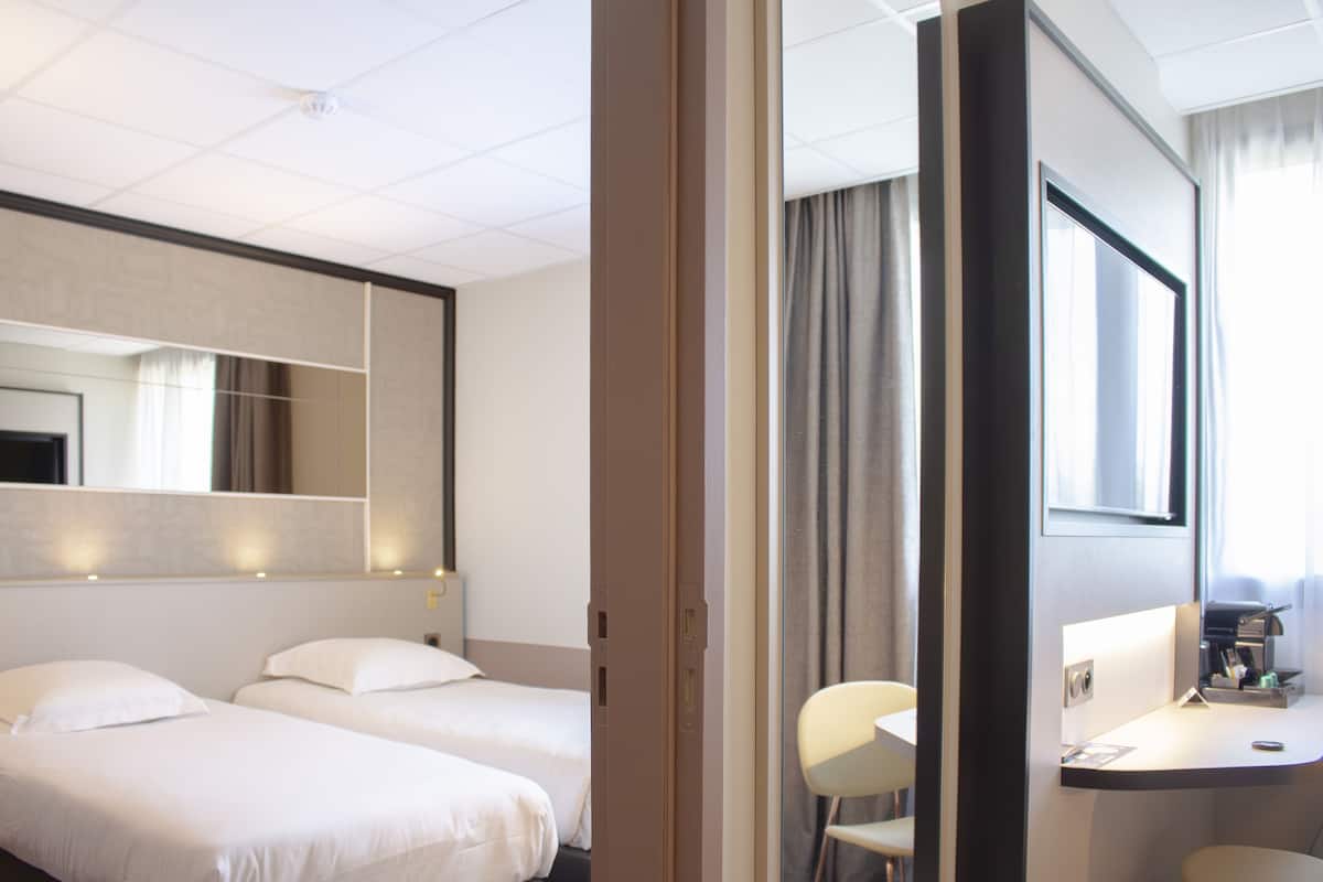 A hotel room with two beds, a desk with a chair, a mirror, and a window with curtains.