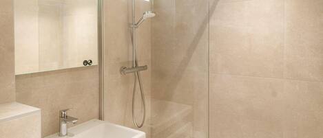 Un baño moderno con ducha envuelta en vidrio, un lavabo blanco y un espejo con luz superior.