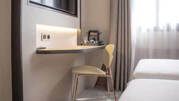 A hotel room with a bed, a desk with a chair, a coffee machine, and a TV mounted on the wall.