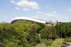 A modern stadium with a unique curved roof, surrounded by lush greenery and a clear sky. - Brit Hotel Nantes La Beaujoire Parc Expo (Nantes)