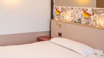 Ein Hotelzimmer mit einem Bett, einem roten Sessel, einem Wandspiegel und einem Blumenmuster an der Tapete.
