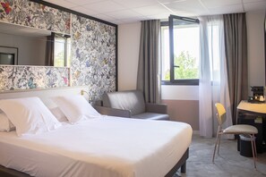 A hotel room with a large bed, a desk, a chair, and a window with curtains. - Brit Hotel Nantes La Beaujoire Parc Expo (Nantes)