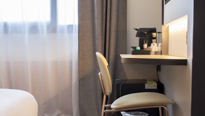 A hotel room with a bed, a desk with a coffee machine, a chair, a trash bin, and a large window with curtains. - Brit Hotel Nantes La Beaujoire Parc Expo (Nantes)