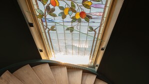 Un escalier en colimaçon avec des marches en bois et des balustrades noires, menant à un vitrail orné de motifs floraux.