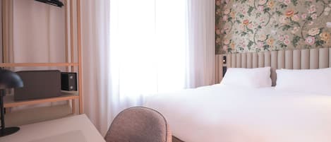 Habitación de hotel con cama, escritorio, silla, perchero y papel tapiz floral.