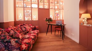 Une pièce comprenant un canapé à motifs floraux, un bureau avec un ordinateur portable et une étagère remplie d’objets décoratifs.
