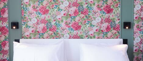 A hotel room with a floral wallpaper, a bed with white linens, and two wall-mounted light fixtures.