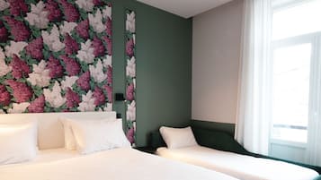 A hotel room with two beds, a floral wall mural, a large window with curtains, and a green accent wall.