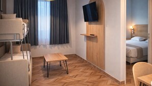 A hotel room with bunk beds, a TV mounted on a wooden panel, a small table, and a chair.