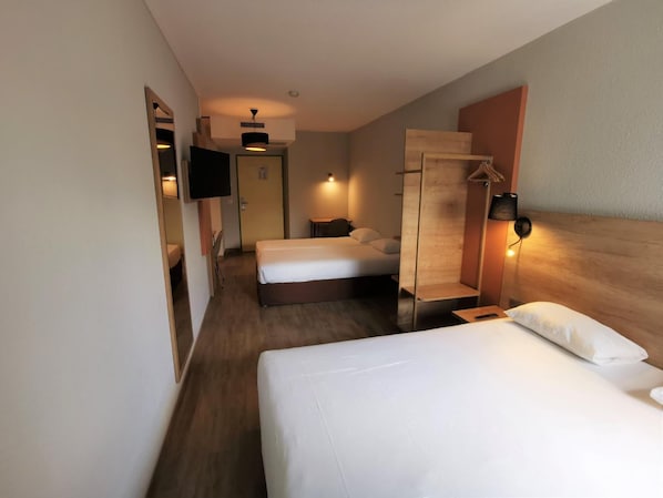 Habitación de hotel con dos camas, televisor, armario de madera y lámpara de pared.