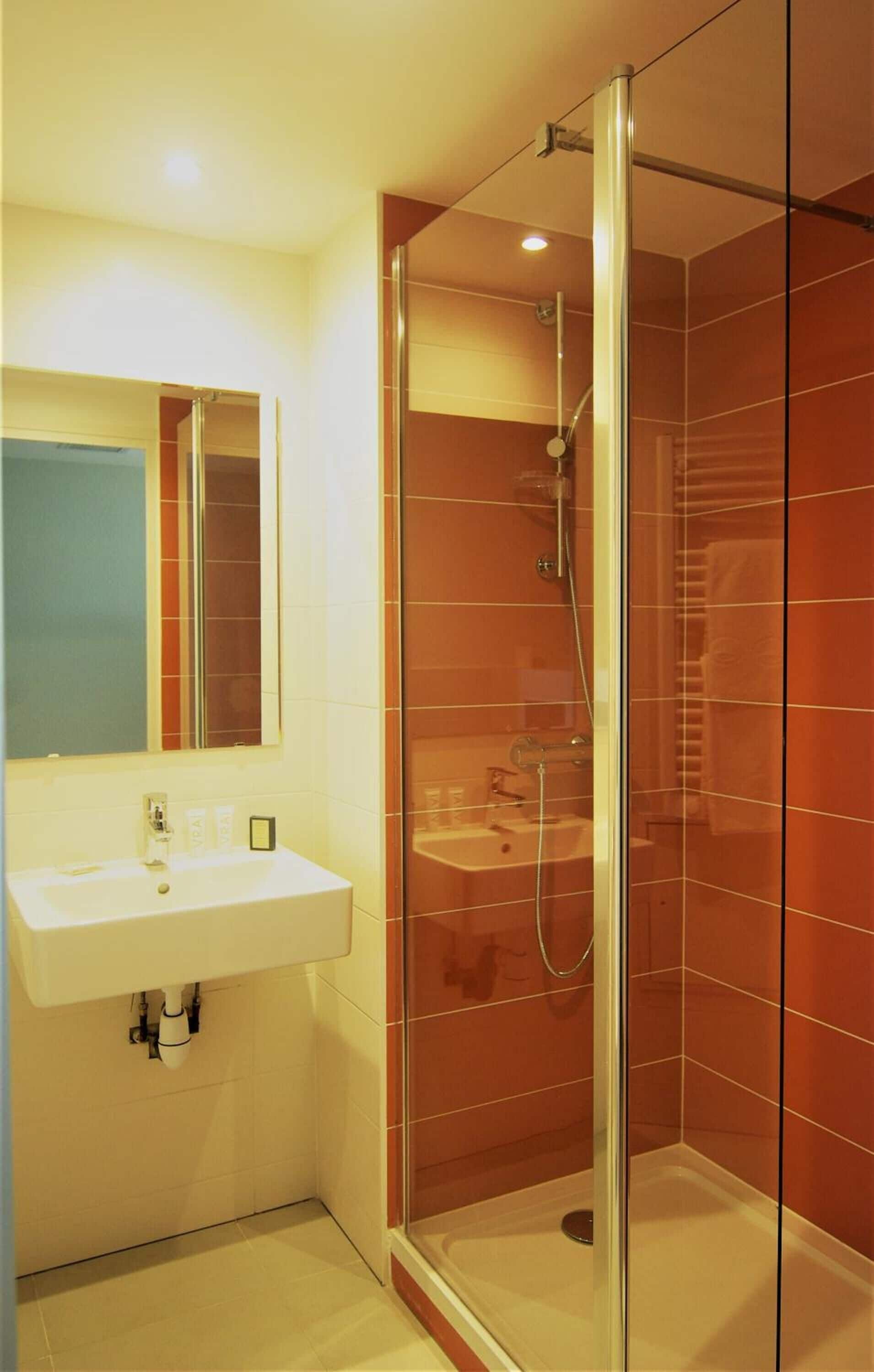 Une salle de bain moderne avec une douche à parois de verre, un lavabo blanc et un miroir au-dessus.